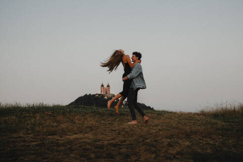 Seitenansicht eines jungen Paares bei einem Spaziergang in der Natur in der Abenddämmerung auf dem Lande, das sich umarmt. - HPIF07172