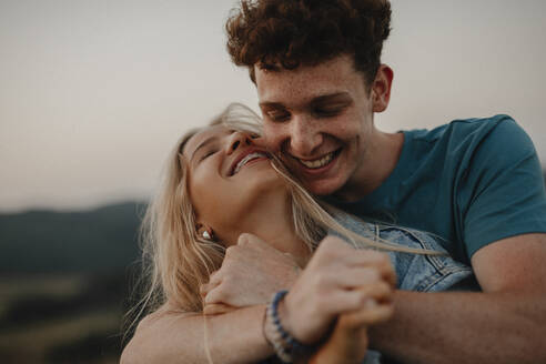 Side view of young couple on a walk in nature at sunset in countryside, hugging and having fun. - HPIF07176