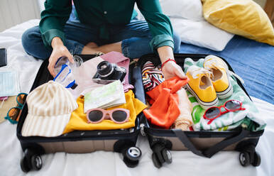 Unrecognizable young woman with suitcase packing for holiday at home, coronavirus concept. - HPIF07223