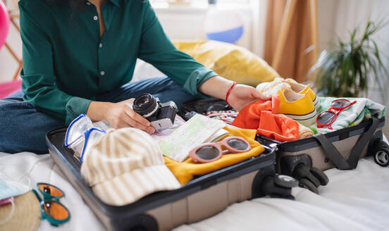 Unrecognizable young woman with suitcase packing for holiday at home, coronavirus concept. - HPIF07224