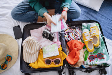 Unrecognizable young woman with suitcase packing for holiday at home, coronavirus concept. - HPIF07225