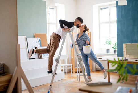Happy mid adults couple kissing when painting indoors at home, relocation and diy concept. - HPIF07248