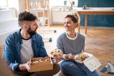 Mid adults couple eating lunch indoors at home, relocation, diy and food delivery concept. - HPIF07266