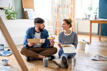 Mid adults couple eating lunch indoors at home, relocation, diy and food delivery concept. - HPIF07267