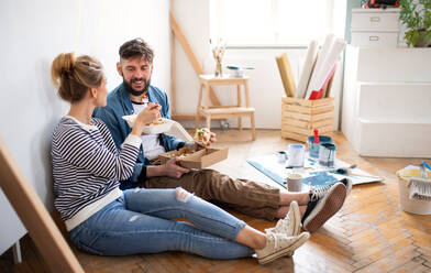 Mid adults couple eating lunch indoors at home, relocation, diy and food delivery concept. - HPIF07268