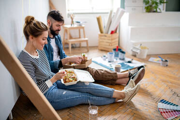 Mid adults couple eating lunch indoors at home, relocation, diy and food delivery concept. - HPIF07269