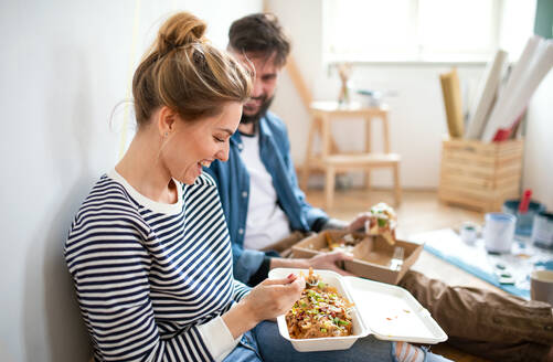 Mid adults couple eating lunch indoors at home, relocation, diy and food delivery concept. - HPIF07270