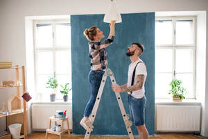 Happy mid adults couple changing light bulb indoors at home, relocation and diy concept. - HPIF07271
