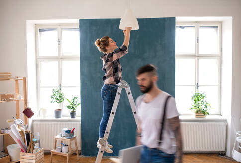 Happy mid adults couple changing light bulb indoors at home, relocation and diy concept. - HPIF07275