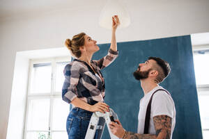 Happy mid adults couple changing light bulb indoors at home, relocation and diy concept. - HPIF07287