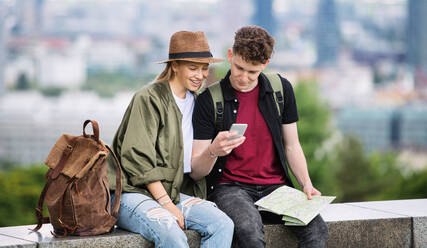 Porträt eines jungen Paares mit Stadtplan im Urlaub, das ein Smartphone benutzt. - HPIF07294