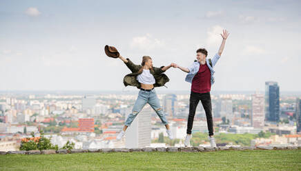 Ein fröhliches junges Paar, das in der Stadt im Urlaub ist und springt, im Hintergrund die Stadtlandschaft. - HPIF07297