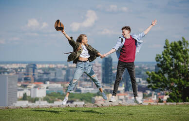 Ein fröhliches junges Paar, das in der Stadt im Urlaub ist und springt, im Hintergrund die Stadtlandschaft. - HPIF07299