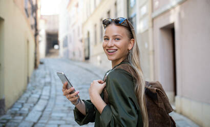 Porträt einer jungen Frau, die im Urlaub in der Stadt ein Smartphone benutzt und in die Kamera schaut. - HPIF07305