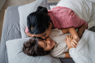 A top view of Indian mother hugging and kissin her little son lying in bed at home. - HPIF07331