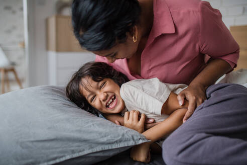 A happy mother tickling her little son when waking him up in morning. - HPIF07332