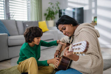A little multiracial boy learning to play the guitar with his mother at home. - HPIF07364