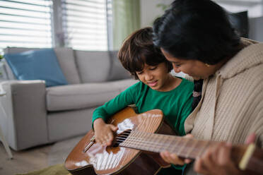 A little multiracial boy learning to play the guitar with his mother at home. - HPIF07365