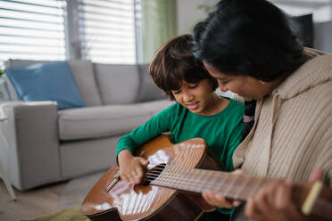 Ein kleiner Junge verschiedener Rassen, der mit seiner Mutter zu Hause Gitarre spielen lernt. - HPIF07365