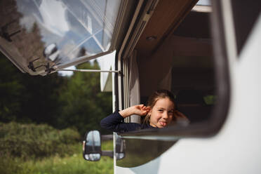 Ein kleines Mädchen, das aus dem Fenster des Wohnwagens schaut und Grimassen schneidet, Familienurlaub. - HPIF07392