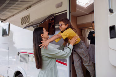 Eine Mutter mit ihren Töchtern steht mit ihrem Auto auf einem Campingplatz in der Abenddämmerung, Familienurlaub mit dem Wohnwagen. - HPIF07396