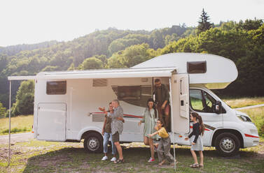 Eine Mehrgenerationen-Familie, die aus dem Auto aussteigt und in der Natur mit dem Wohnwagen Urlaub macht. - HPIF07402