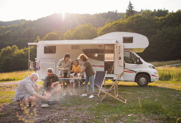 A multi-generation family sitting and eating outdoors by car, caravan holiday trip. - HPIF07413