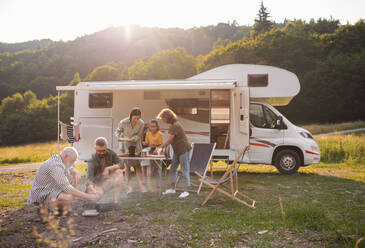 Eine Mehrgenerationen-Familie, die mit dem Auto im Freien sitzt und isst, eine Urlaubsreise mit dem Wohnwagen. - HPIF07413