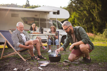 Eine Mehrgenerationen-Familie bei der Zubereitung von Speisen auf dem Grill im Auto, Urlaubsreise mit dem Wohnwagen. - HPIF07414