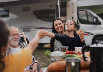 Eine Mehrgenerationen-Familie, die mit dem Auto im Freien sitzt und isst, eine Urlaubsreise mit dem Wohnwagen. - HPIF07417