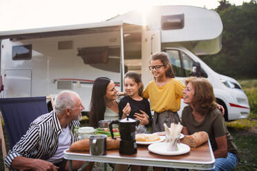 Eine Mehrgenerationen-Familie, die mit dem Auto im Freien sitzt und isst, eine Urlaubsreise mit dem Wohnwagen. - HPIF07419