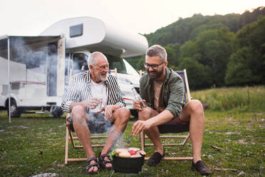 Ein reifer Mann mit seinem älteren Vater unterhält sich auf einem Campingplatz im Freien beim Grillen auf einer Wohnwagenreise. - HPIF07422