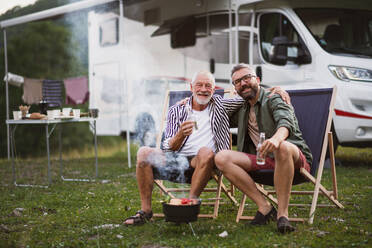 Ein reifer Mann mit älterem Vater schaut in die Kamera auf dem Campingplatz im Freien, Grill auf Caravan-Urlaub Reise. - HPIF07425