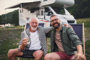 Ein reifer Mann mit älterem Vater schaut in die Kamera auf dem Campingplatz im Freien, Grill auf Caravan-Urlaub Reise. - HPIF07426