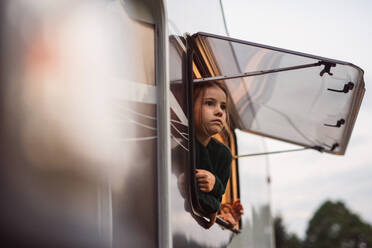 Ein kleines Mädchen schaut durch das Fenster des Wohnwagens, Familienurlaub. - HPIF07440