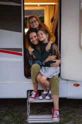 Glückliche Mutter mit Töchtern im Auto auf dem Campingplatz in der Abenddämmerung, Familienurlaub mit dem Wohnwagen. - HPIF07441