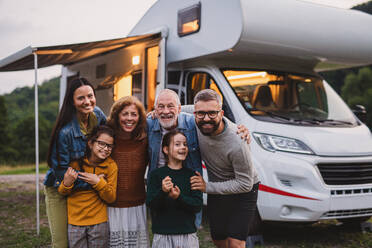 Eine Mehrgenerationen-Familie, die in der Abenddämmerung im Freien auf die Kamera schaut, Urlaub im Wohnwagen. - HPIF07451