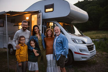 Ein Porträt einer Mehrgenerationen-Familie, die in die Kamera schaut und lächelt, draußen in der Abenddämmerung, Urlaub im Wohnwagen. - HPIF07452