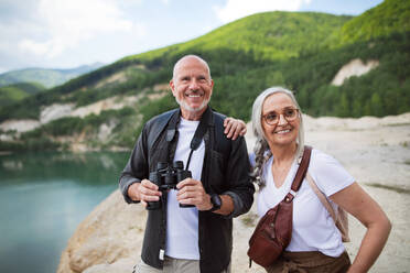 Ein glückliches älteres Ehepaar auf einer Wandertour im Sommerurlaub, das ein Fernglas benutzt. - HPIF07460