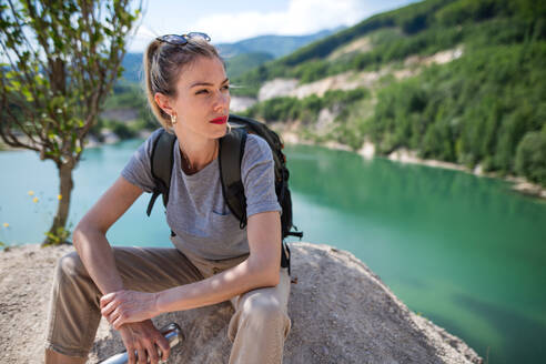 Eine mittelgroße erwachsene Touristin auf Wandertour im Sommerurlaub, die sich am See ausruht. - HPIF07464