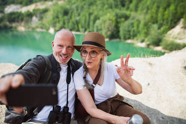 Senior couple enjoying summer hike, capturing memories with a silly selfie - HPIF07467