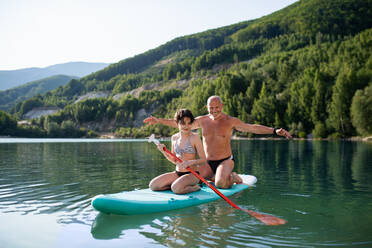 Ein glückliches Mädchen mit Großvater im Sommerurlaub am See beim Paddelboarding. - HPIF07477