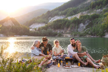 A happy multigeneration family on summer holiday trip, barbecue by lake at sunset. - HPIF07488