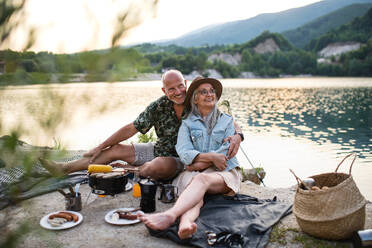 Portrait of happy senior couple resting on summer holiday trip, barbecue by lake. - HPIF07495