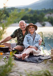 Portrait of happy senior couple resting on summer holiday trip, barbecue by lake. - HPIF07496