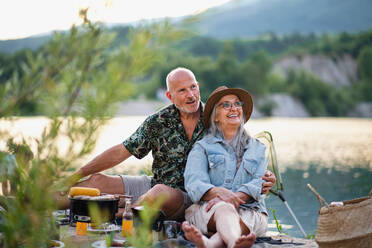 Porträt eines glücklichen älteren Paares, das sich auf einem Sommerurlaubsausflug ausruht und am See grillt. - HPIF07497