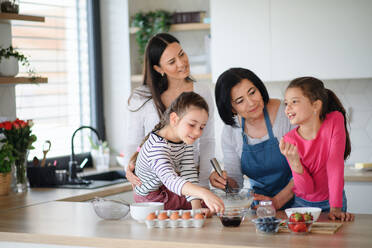 Glückliche kleine Mädchen mit Mutter und Großmutter bei der Zubereitung von Pfannkuchenteig zu Hause, beim Kochen. - HPIF07512