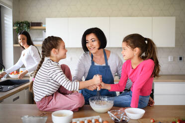 Glückliche kleine Mädchen mit Mutter und Großmutter bei der Zubereitung von Pfannkuchenteig zu Hause, beim Kochen. - HPIF07513