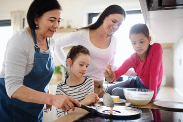 Glückliche kleine Mädchen mit Mutter und Großmutter, die zu Hause Pfannkuchen backen und kochen. - HPIF07516