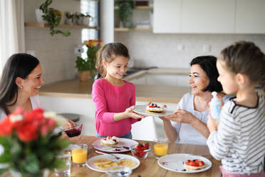 Glückliche kleine Mädchen mit Mutter und Großmutter essen Pfannkuchen zu Hause beim Mittagessen. - HPIF07518